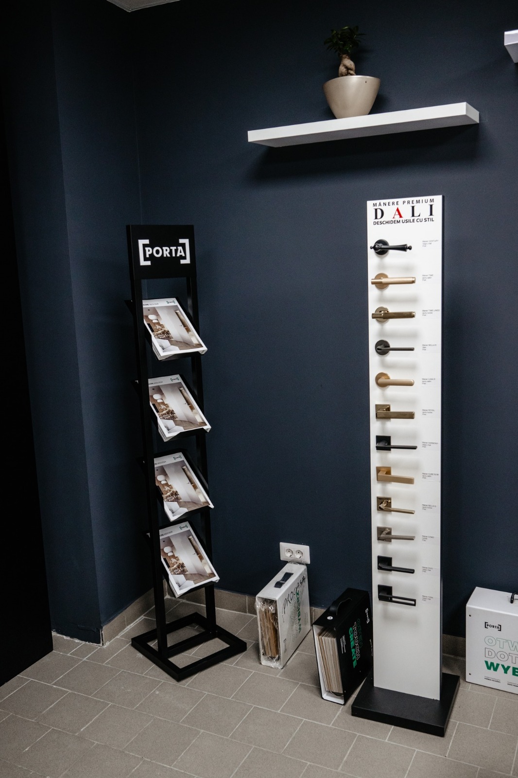 Coloana cu mânere premium DALI și rastelul cu cataloage Porta, pe peretele antracit din showroom-ul de uși din Bacău
